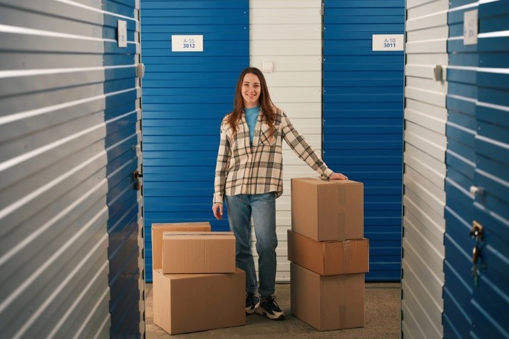 woman in front of a storage unit with blue doors and boxes next to her