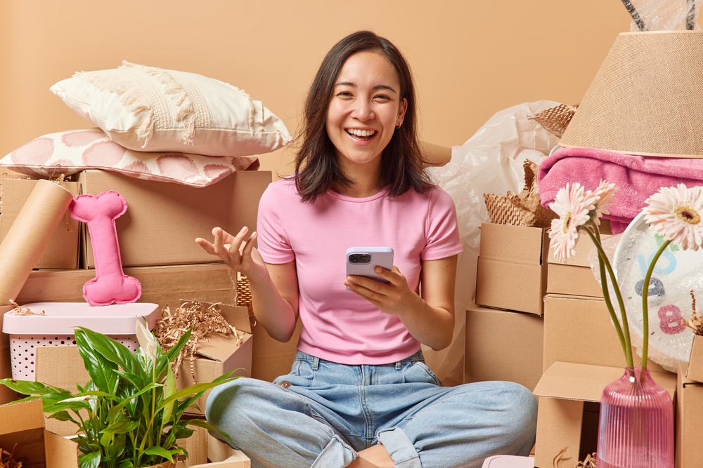 Happy young woman on phone while sitting near a pile of boxes